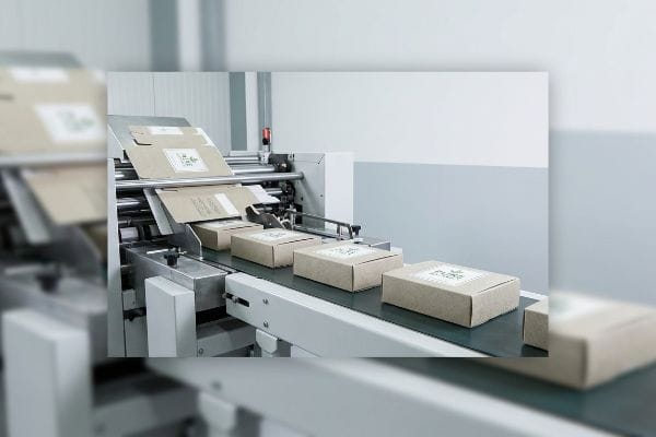 Kraft paper custom soap boxes with green labels moving along an automated packaging machine conveyor belt.