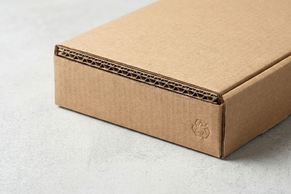 Brown kraft corrugated box close-up, showing fluted cardboard layers and a debossed recycling symbol, highlighting eco-friendly packaging.
