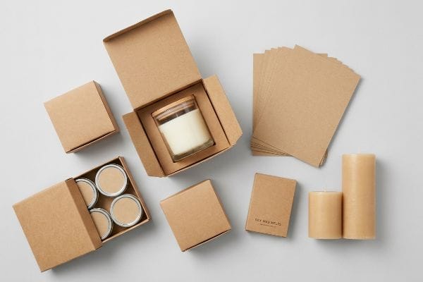 Overhead flat lay of eco-friendly Kraft packaging with glass jar candle, soy wax melts, tin travel candles, and pillar candles.