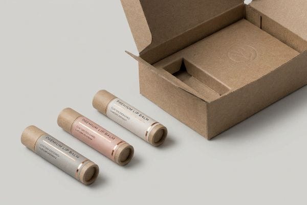 Kraft paper Premium Lip Balm tubes with rose gold accents beside an open, empty cardboard box.