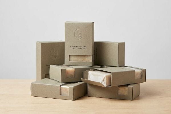 Handmade Soap Packaging Stack Multiple kraft paper handmade soap boxes stacked, some open revealing natural soap bars, featuring a debossed leaf logo and "Handmade Soap Certified Organic" text.
