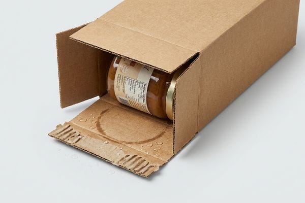 Corrugated kraft paper box with water droplets and a circular stain on its bottom flap, illustrating moisture absorption and packaging failure around a glass jar.
