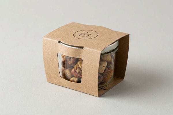 Kraft Jar Sleeve Packaging Brown kraft paperboard sleeve packaging encloses a glass jar of mixed nuts, featuring a die-cut window and a minimalist crown logo.