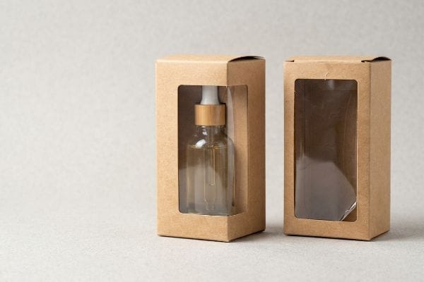 Two Kraft paper window boxes, one displaying a clear dropper bottle with a bamboo-style cap, the other empty, on a light background.