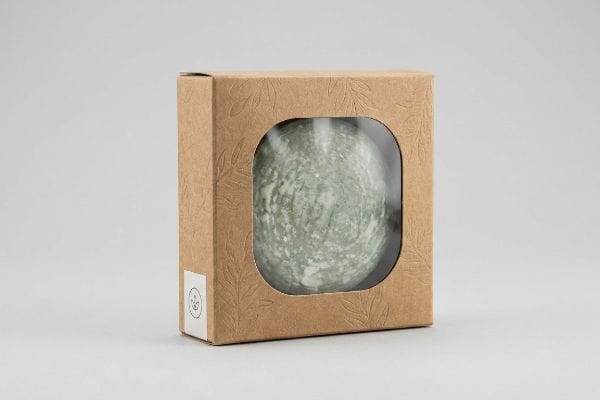 Kraft paper box with embossed leaves, clear window showcasing a round green artisanal soap bar.