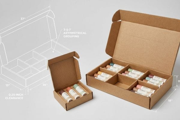 Brown corrugated boxes with lip balm sets, featuring 3-5-7 Asymmetrical Grouping and 0.25-inch clearance, showing dimensions.