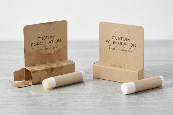 Kraft paper lip balm packaging displays a tube with melted product spilled, next to an intact package, both featuring "Custom Formulation" and "Premium Protection" text.