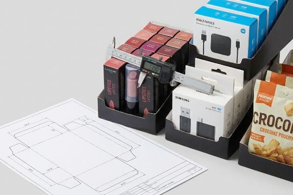 Caliper Measuring Product Dimensions A digital caliper measures a Lipstick box at 17.90 in a black retail display tray, alongside Samsung electronics and Hony Originals Croco snacks, with a dieline.