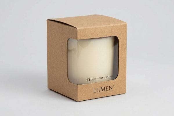 Brown kraft paperboard candle box with a die-cut window revealing a white candle, featuring 'Lumen' brand and '100% Curbside Recyclable' text.