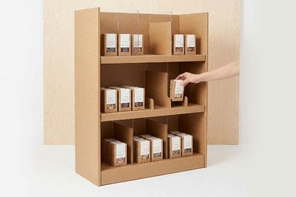 Modular Display Restocking Brown corrugated cardboard retail display with modular SKU dividers, a hand placing product boxes, demonstrating ergonomic clearance for efficient restocking.