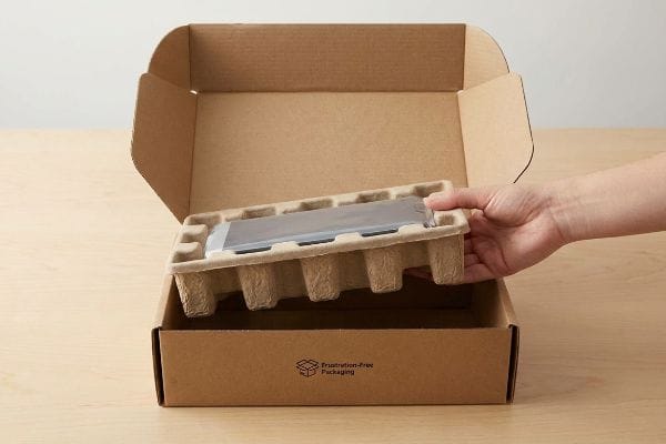 A hand lifts a product in a molded pulp tray from a Frustration-Free Packaging cardboard box, highlighting sustainable unboxing.
