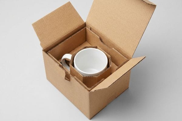Brown corrugated cardboard box with an E-flute insert protecting a white ceramic mug, demonstrating kinetic suspension packaging.