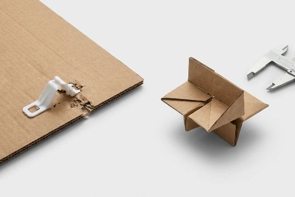 Damaged corrugated cardboard with plastic clip, beside an origami friction lock and caliper.
