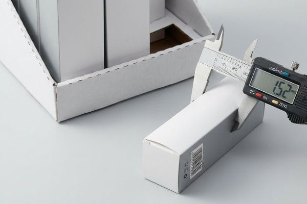 A digital caliper precisely measures a white folding carton, displaying 1.52 mm, crucial for accurate packaging dimensions.