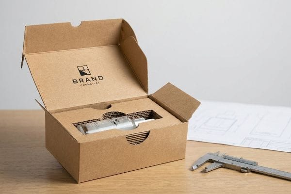 Kraftpapierkarton mit einer Flasche von Brand Cosmetics in einem ausgestanzten Einsatz, daneben ein Messschieber und eine Bauzeichnung.