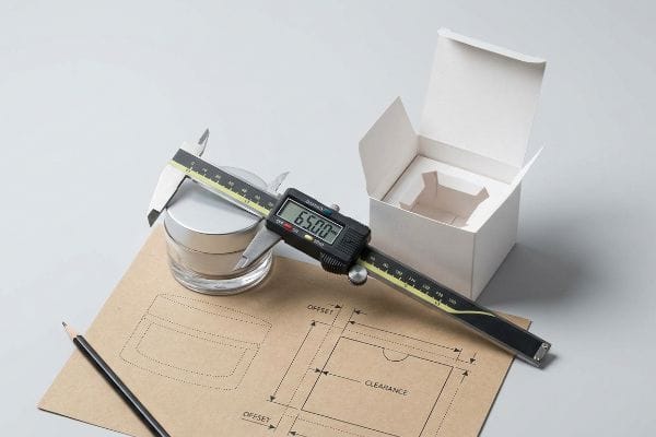 Cream Jar Dimensions Measuring a cream jar's diameter with a digital caliper displaying 65.00, alongside technical packaging drawings for Offset and Clearance, and an open white box.