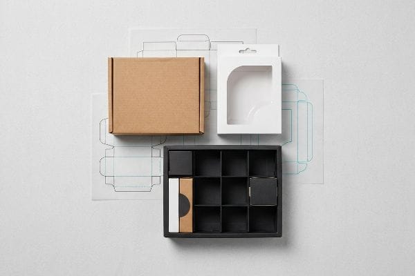 Overhead view of bespoke packaging: brown mailer, white window carton, black display tray with dividers, and die-cut templates.