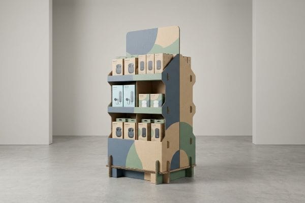 Cardboard POP Display A corrugated cardboard point-of-purchase display with blue, green, and beige abstract patterns showcases various product boxes in a minimalist retail setting.