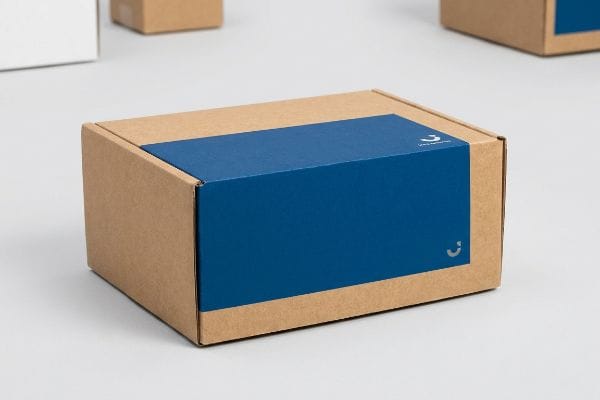 A brown virgin kraft cardboard box with a deep blue Pantone spot color band, featuring the 'Unpacked' logo.