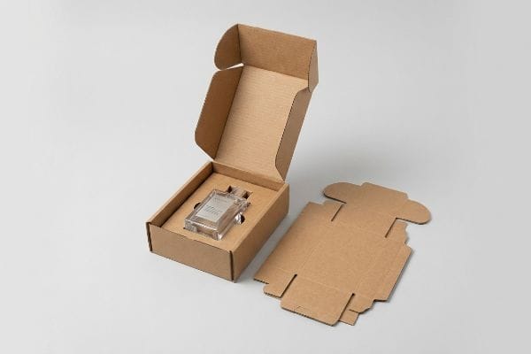 Custom Die-Cut Packaging An open die-cut brown corrugated box securely holding a clear perfume bottle, with flat die-cut cardboard packaging pieces beside it.