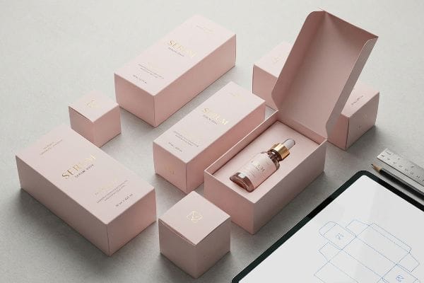 Custom Pink Serum Boxes An arrangement of custom pink paperboard cosmetic boxes with gold foil 'Serum Aqua' branding, one open revealing a serum bottle, next to a tablet showing a packaging die-line.