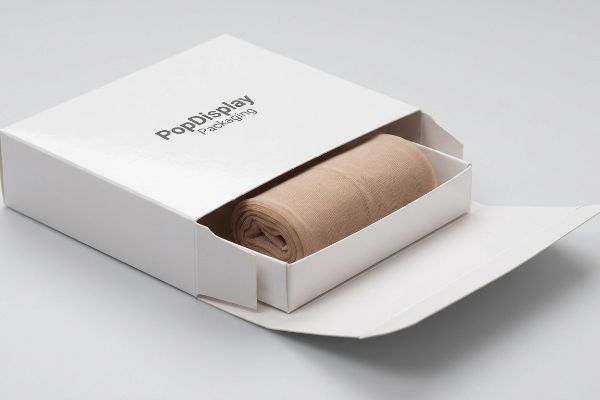 An elegant white PopDisplay Packaging hosiery box, partially open, showcases neatly rolled nude hosiery.