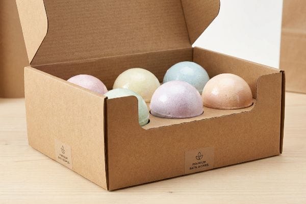 Premium Bath Bomb Box An open corrugated cardboard display box holds six pastel bath bombs, featuring a 'Premium Bath Bombs' label.