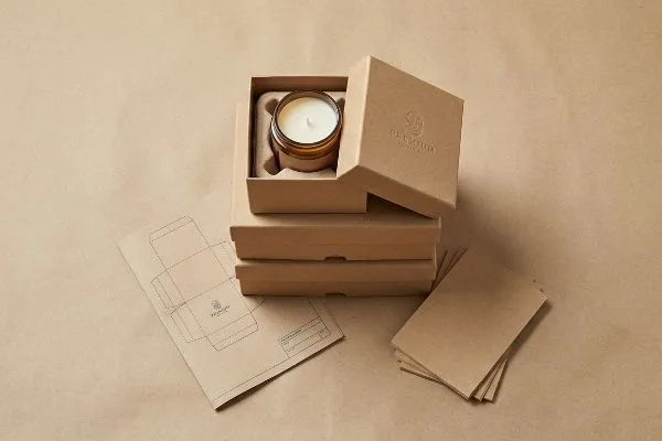 Emballage de bougie Kraft de qualité supérieure Une boîte à bougie ouverte en kraft, portant l'inscription « Premium » en relief, présente une bougie en pot de verre ambré, avec des boîtes empilées, un gabarit plat et des cartes en kraft.
