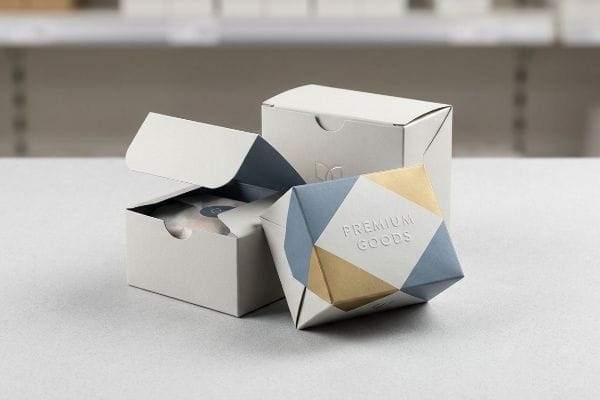 Premium Goods Packaging Modern retail display features two white folding cartons, one open, alongside a geometric Premium Goods package with gold and blue patterns.