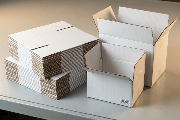 Premium White Corrugated Boxes Displaying white corrugated boxes, including flat-packed stacks and two assembled open boxes, one with "Premium SBS Corrugated" text.
