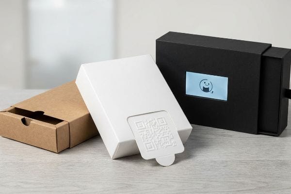 Interactive Packaging Solutions Interactive packaging showcases a white box with a QR code pull-tab, a black box with an embedded LCD screen, and a brown pull-out tray box.