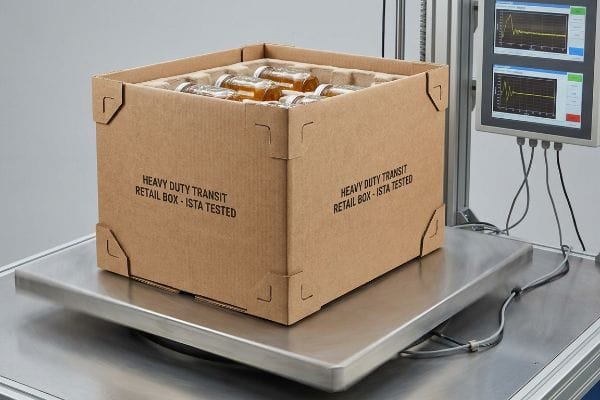 Brown corrugated Heavy Duty Transit Retail Box - ISTA Tested, packed with glass bottles, on a kinetic vibration table with a performance monitor.