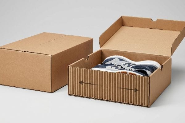 Vertical Flute Shoe Packaging Corrugated cardboard box with vertically aligned flutes holding blue and white sneakers, positioned beside a closed shipping carton.