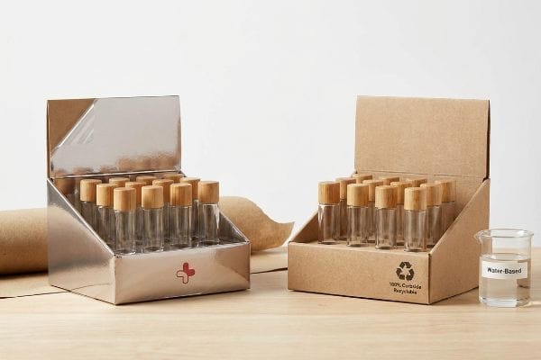 Shiny silver display box with a red cross logo, holding clear glass vials with natural wooden caps, on a light wooden surface.