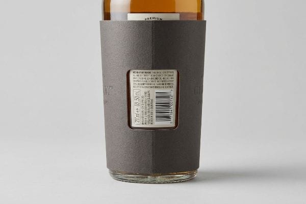 Bottle Sleeve Compliance Window Dark gray paperboard sleeve with a die-cut window, revealing a white bottle label showing "120 ml e 39.50 fl oz", a barcode, and "Premium" text for legal compliance.