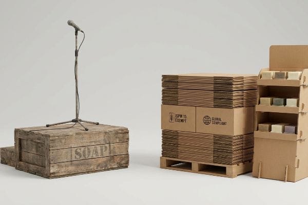Rustic wooden Soap crate with microphone, alongside corrugated boxes marked ISPM 15 Exempt and Global Compliant, and a cardboard soap display.