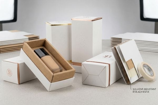 Weiße Kosmetikverpackung mit Goldfolie, eine geöffnete Schachtel, die eine Foundation-Flasche freigibt, und ein Karton mit der Aufschrift „Lösungsmittelbeständiger EVA-Klebstoff“.