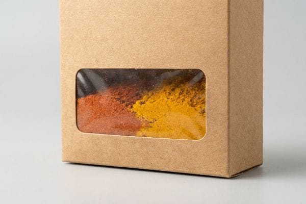 Spice Window Box Packaging Brown Kraft paper box with a clear window patch displaying reddish-orange paprika and yellow turmeric spices, highlighting premium spice packaging.