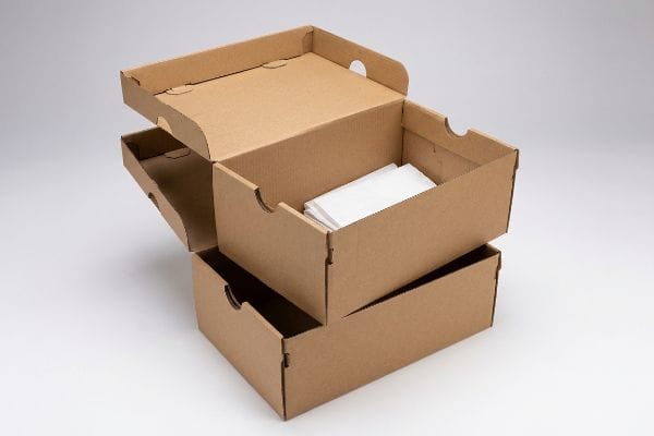 Stacked open brown corrugated cardboard shoe boxes, the top one holding white tissue paper, perfect for footwear storage.