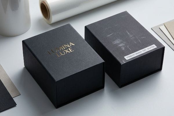 Packaging Scuffing Test Black packaging boxes, one with Lumina Luxe gold foil, the other showing scuffed Standard Varnish Test, highlighting scratch resistance.