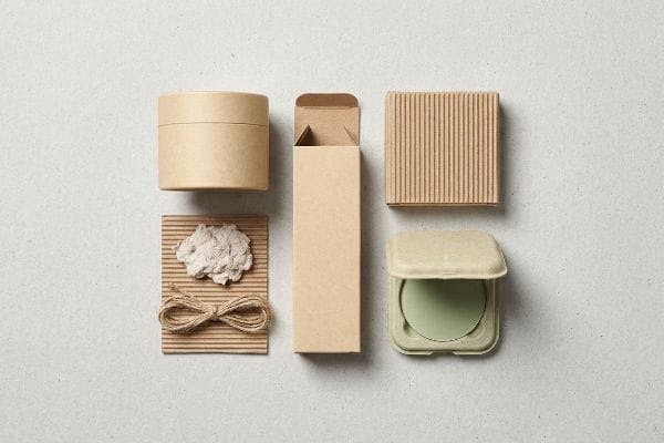 Sustainable Cosmetic Packaging Display An overhead flat lay showcases various sustainable cosmetic packaging components including kraft paper boxes, corrugated cardboard, and a molded fiber compact with a green insert.