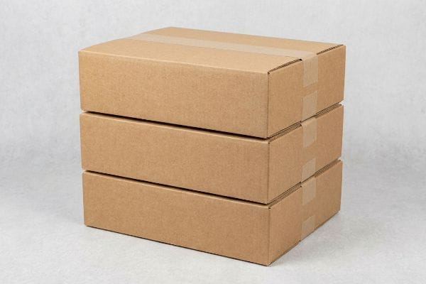 Stacked Plain Cardboard Boxes Three plain brown corrugated cardboard boxes, sealed with tape, stacked neatly on a light gray background, ready for shipping.