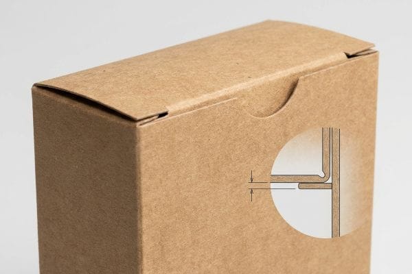 Brown kraft paper tuck box top flap with a circular diagram illustrating caliper compensation for bend allowance in the slot.