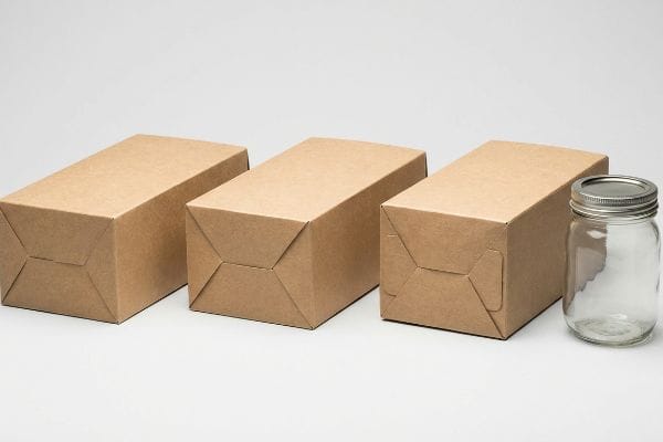 Three rectangular raw Kraft paperboard boxes with tuck-end closures are displayed next to a clear glass mason jar with a silver lid.