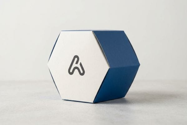 Two-toned white and blue hexagonal packaging box with a stylized A logo, symbolizing balance and visual disruption.