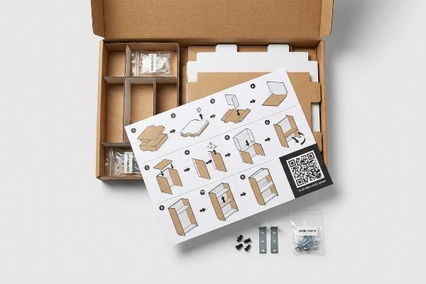 Visual Assembly Instructions Kit White visual assembly instructions with QR code, friction-lock hardware, universal metal brackets, and a 'Spare Parts' bag in an open flat-pack retail display box.