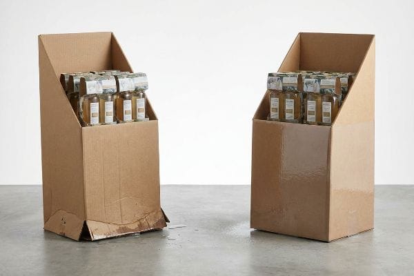 Collapsed Display Stand Brown corrugated cardboard display stand with a water-damaged, collapsed base, spilling liquid onto the concrete floor, filled with beverage bottles.