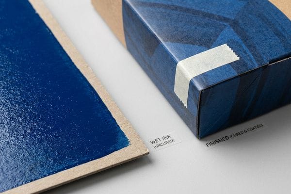 Ink Curing Comparison Wet Ink (Uncured) blue pigment on cardboard contrasts with a Finished (Cured & Coated) blue patterned box, highlighting curing.