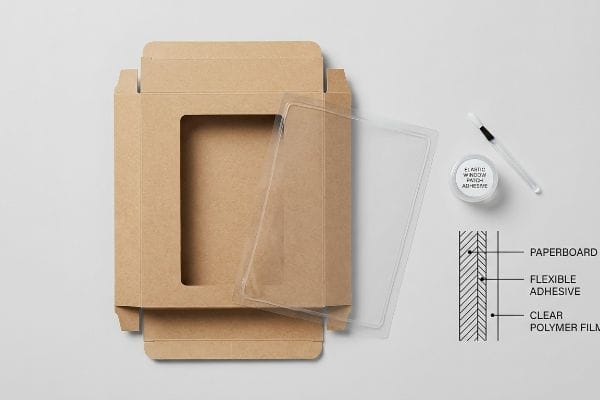 Window Patch Adhesive Kit Unfolded brown paperboard display box with a die-cut window, clear polymer film, Elastic Window Patch Adhesive, and a diagram of Paperboard, Flexible Adhesive, Clear Polymer Film layers.