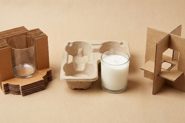 Insertos para envases de velas Elementos de embalaje ecológicos para velas: cartón corrugado troquelado a medida, una bandeja de pulpa moldeada, frascos de vidrio y una vela blanca.